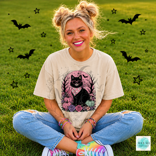 Person sitting on grass with Halloween-themed decorations, wearing a t-shirt with a black cat design.