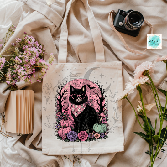 Tote bag with a black cat design on a beige fabric background with flowers and a camera.
