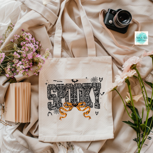Tote bag with Halloween-themed design on a soft fabric background with flowers and a camera.