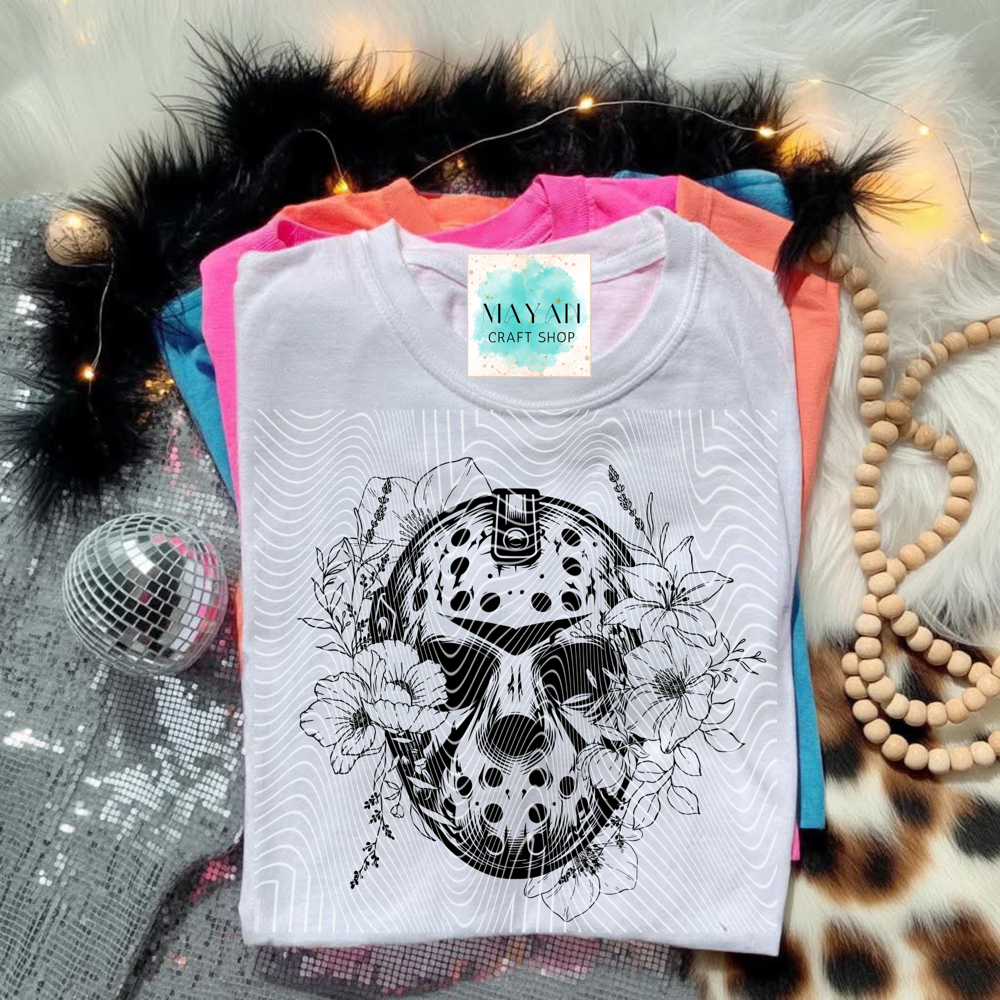 White t-shirt with black graphic design on a colorful stack of shirts.