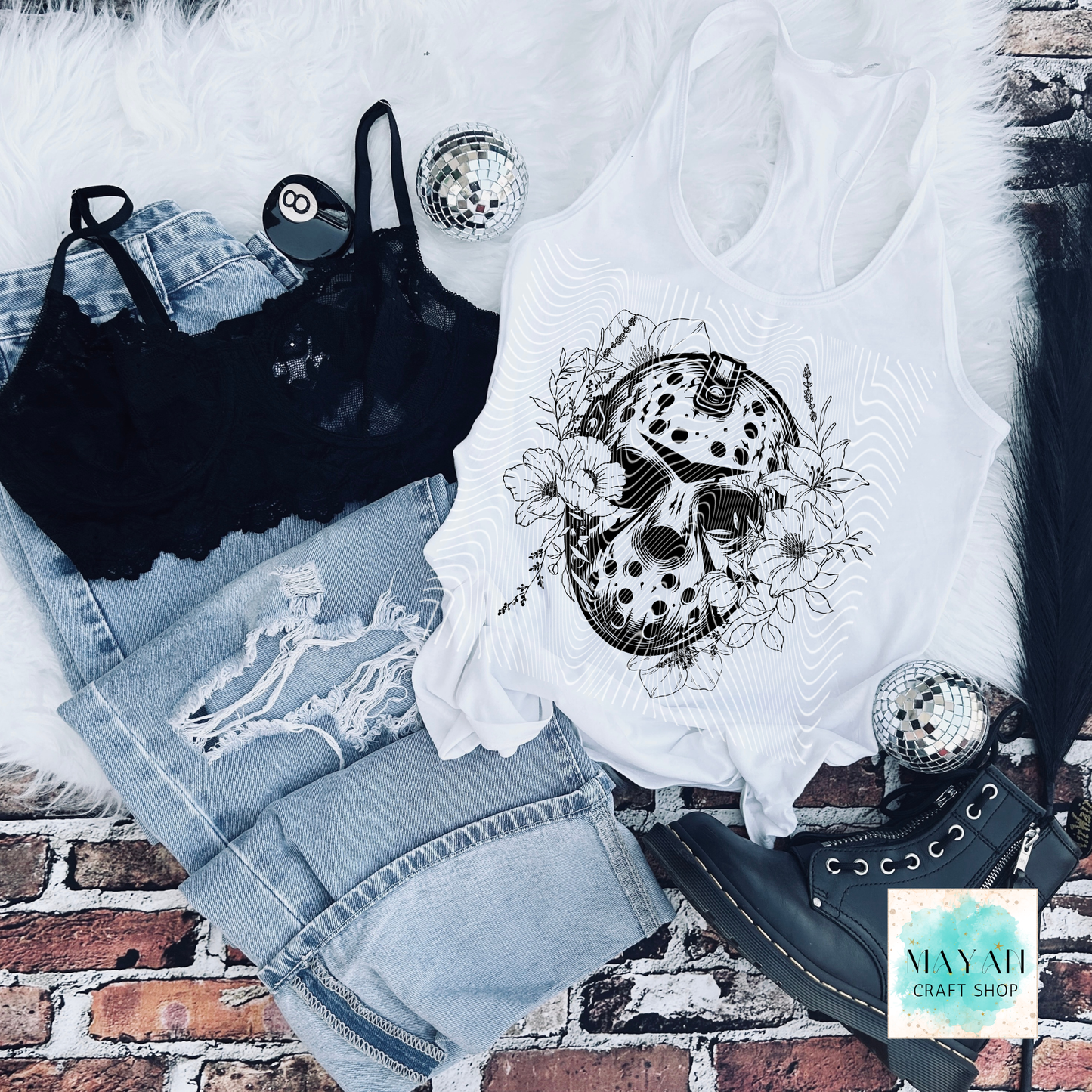 White tank top with decorative design, black bralette, blue jeans, and black shoes on a brick surface.