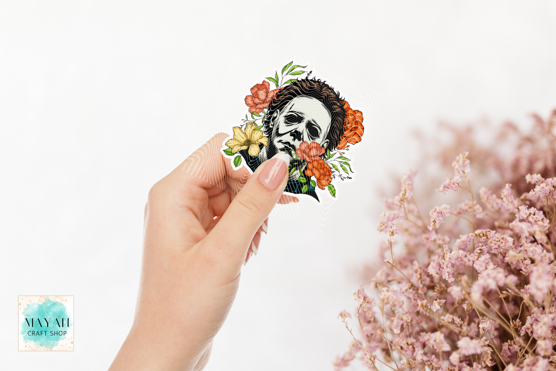 Hand holding a decorative sticker with a skull and floral design on a white background.