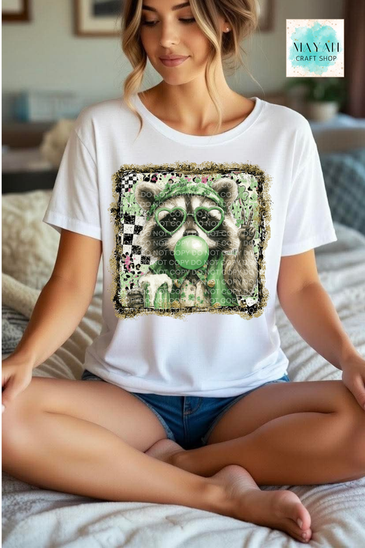 Woman wearing a white t-shirt with a graphic design of a raccoon blowing a bubble, sitting on a bed.