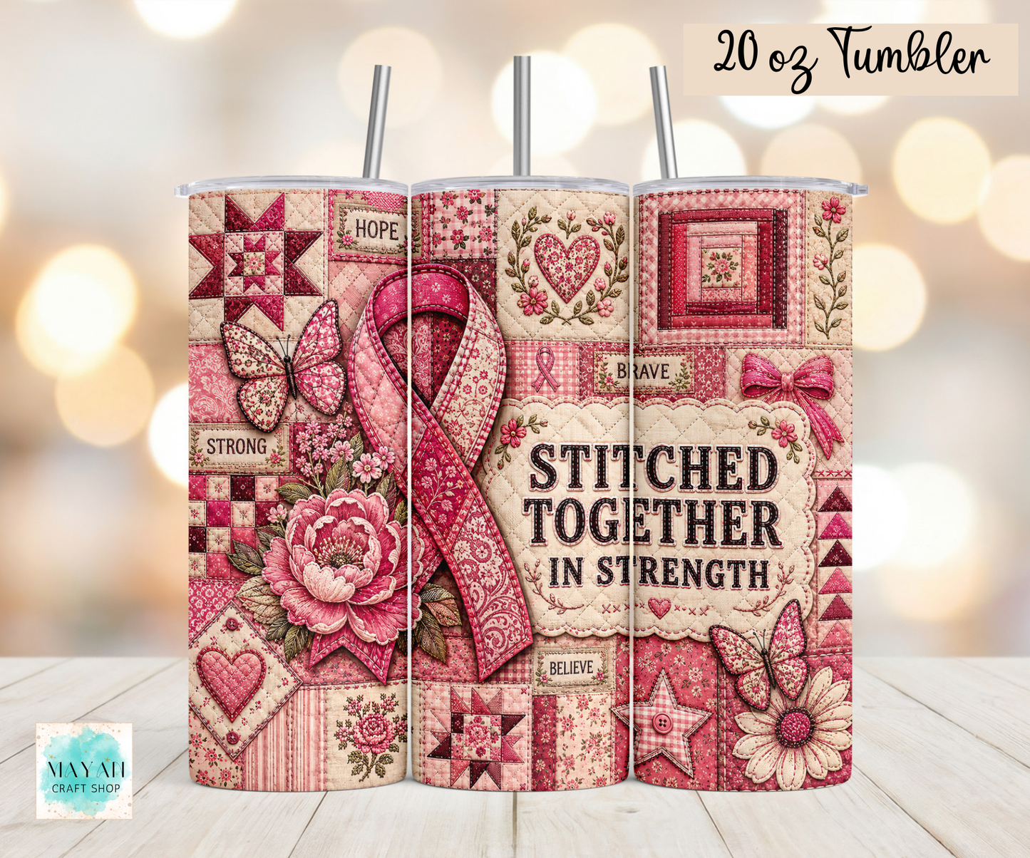 Three 20 oz tumblers with metal straws displayed side-by-side on a light wood surface against a warm bokeh background. The tumblers feature a pink and beige quilted patchwork design with a large pink ribbon, roses, butterflies, and the text 'STITCHED TOGETHER IN STRENGTH' and '20 oz Tumbler'.