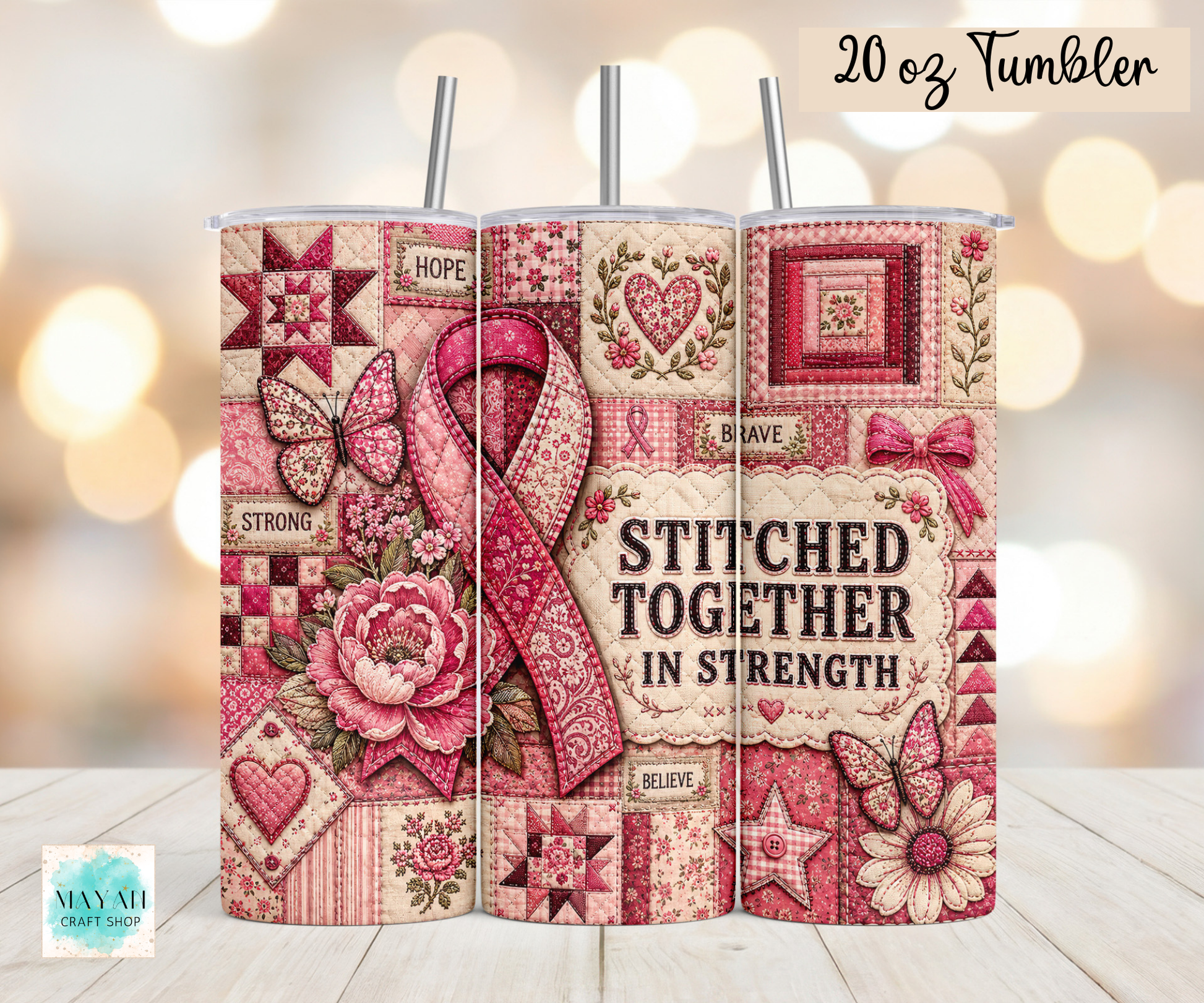 Three 20 oz tumblers with metal straws displayed side-by-side on a light wood surface against a warm bokeh background. The tumblers feature a pink and beige quilted patchwork design with a large pink ribbon, roses, butterflies, and the text 'STITCHED TOGETHER IN STRENGTH' and '20 oz Tumbler'.