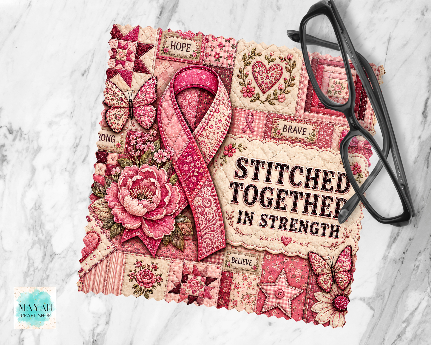 A lens cloth cleaner with a pink and red patchwork design, featuring a large pink ribbon, flowers, butterflies, and the words 'STITCHED TOGETHER IN STRENGTH.' A pair of black eyeglasses rests on the right side, and the item is photographed on a light marble surface.