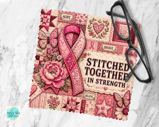 A lens cloth cleaner with a pink and red patchwork design, featuring a large pink ribbon, flowers, butterflies, and the words 'STITCHED TOGETHER IN STRENGTH.' A pair of black eyeglasses rests on the right side, and the item is photographed on a light marble surface.