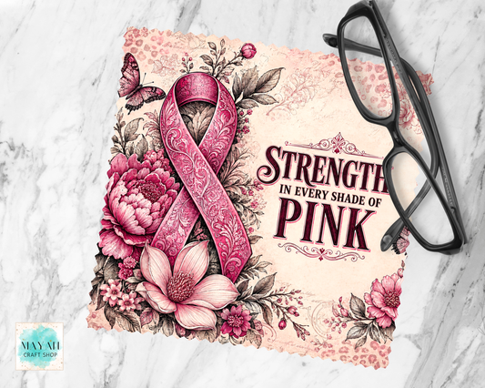 A lens cloth cleaner featuring a pink patterned awareness ribbon, pink flowers, leaves, and the text 'STRENGTH IN EVERY SHADE OF PINK,' styled on a light marble surface with black eyeglasses placed on top. 