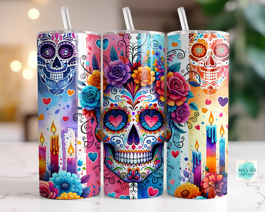 Three colorful tumblers with sugar skull designs on a blurred background