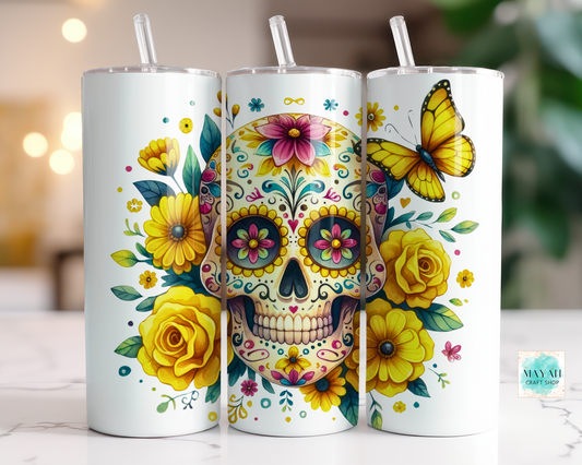 Three white tumblers with colorful sugar skull designs, flowers, and butterflies on a blurred background.