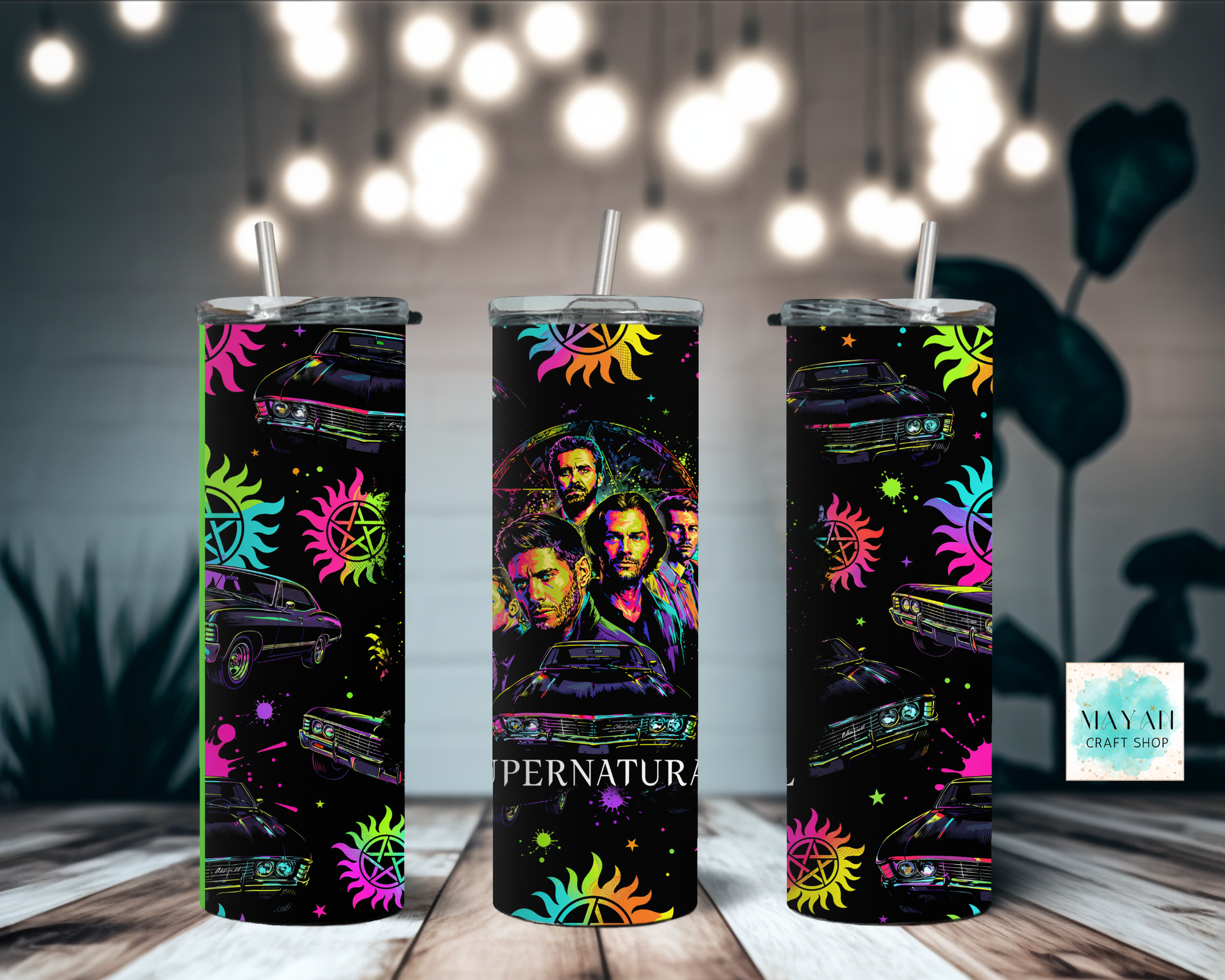 Three colorful tumblers with a design on a wooden surface with blurred lights in the background.