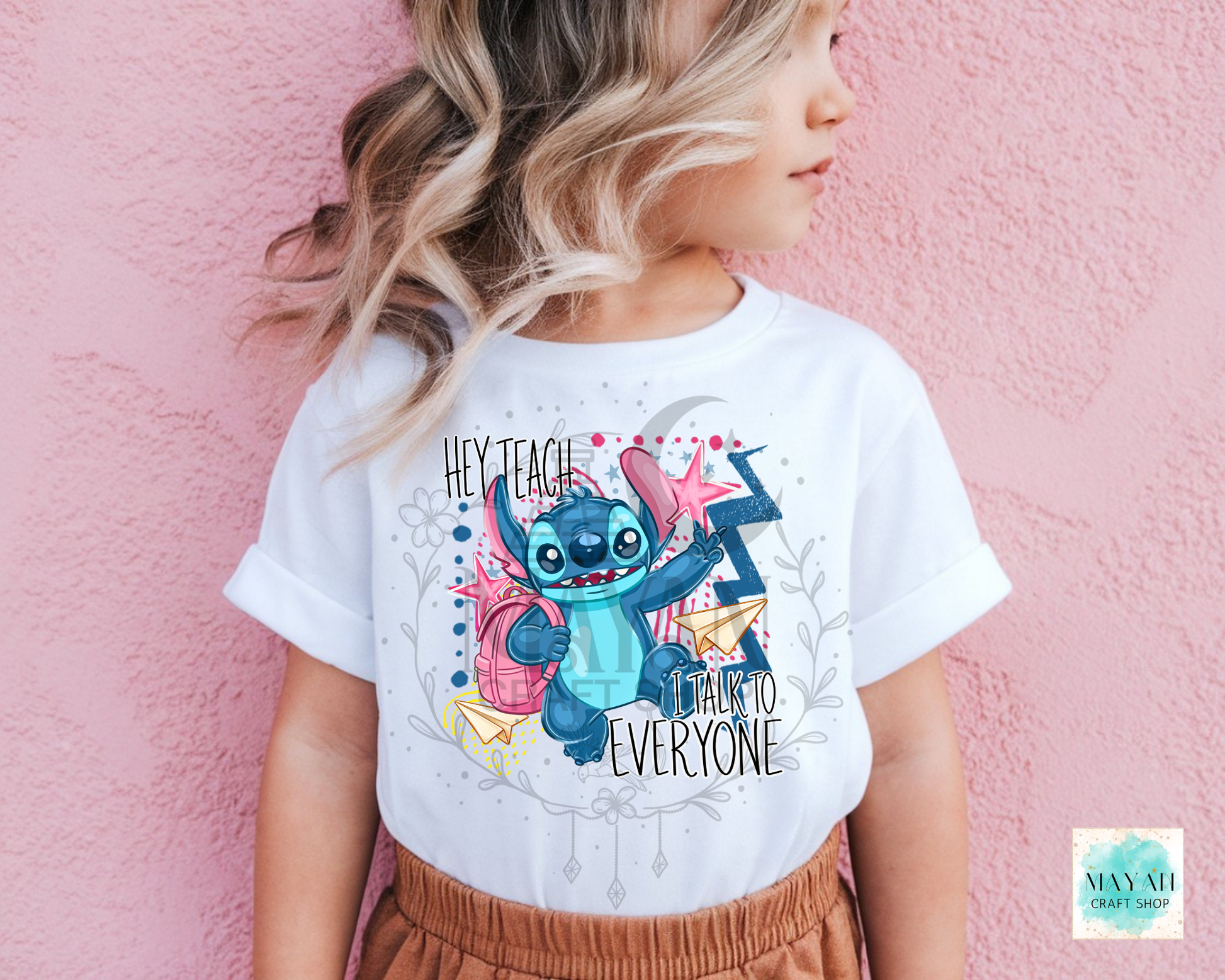 A child wearing a white graphic T-shirt featuring a cartoon with the text 'HEY TEACH ME TO EVERYONE' against a pink textured wall.