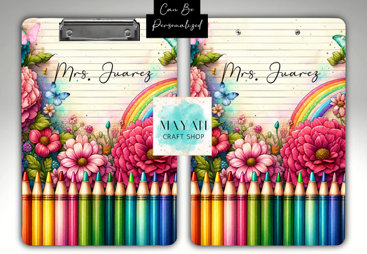 A personalized clipboard cover design shown from the front, featuring a floral and rainbow illustration with rows of colorful crayons along the bottom. The text 'Mrs.