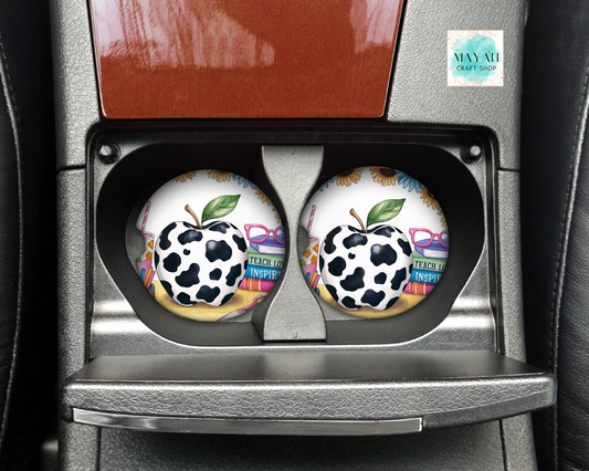 Two cow print coasters in a car cup holder with 'Mayan Craft Shop'