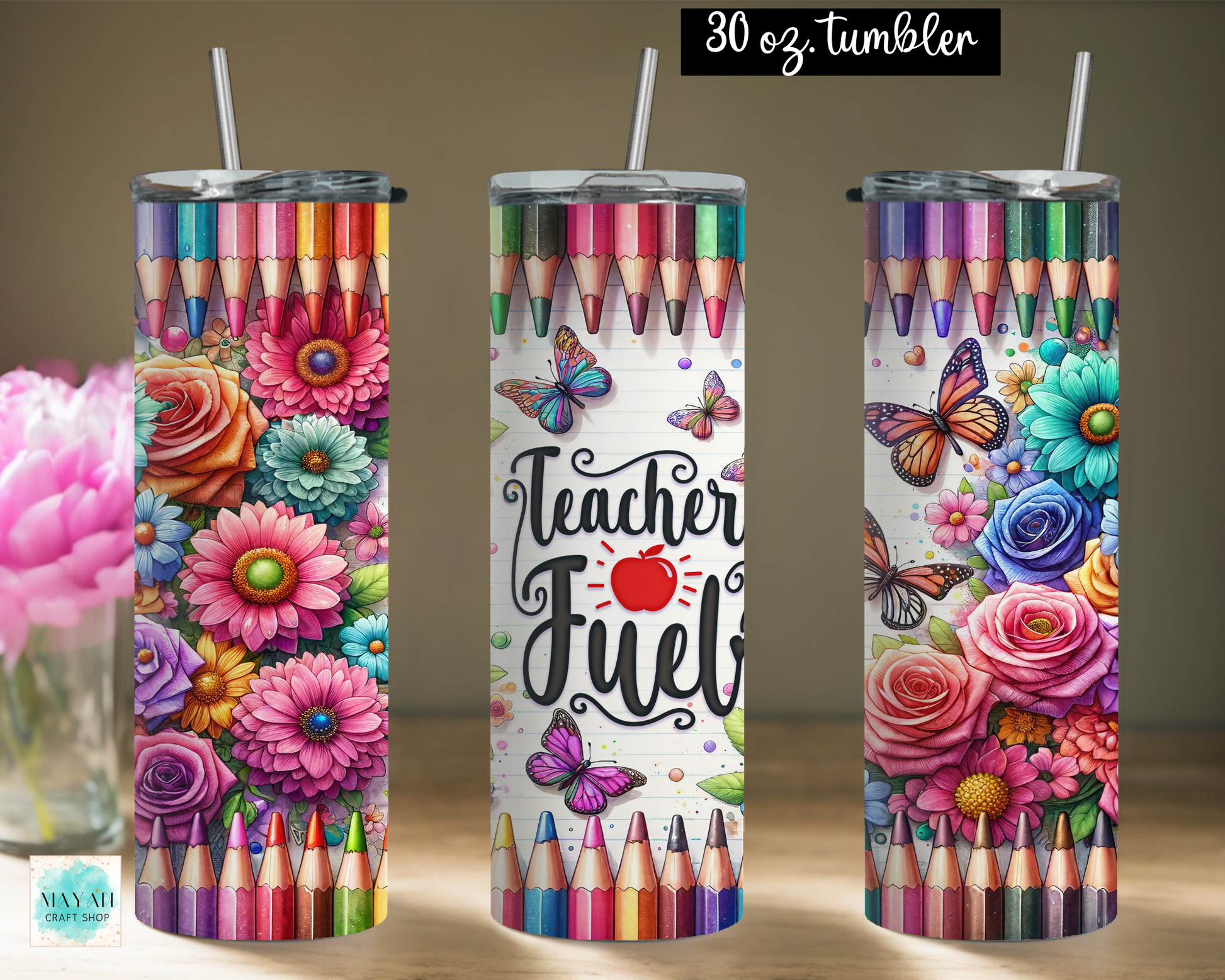 Three tall skinny tumblers with clear straws are shown on a tabletop against a warm beige wall. The tumblers feature colorful printed artwork: rows of colored pencils at the top and bottom, large flowers, butterflies, and one center design with the words 'Teacher Fuel' and a red apple.