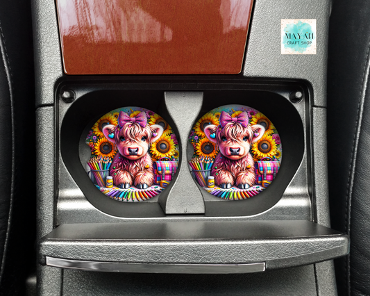 Two colorful car coasters with a cow design in a car cup holder.