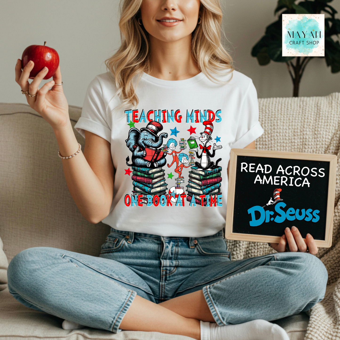Person wearing a reading-themed shirt holding an apple and a sign.