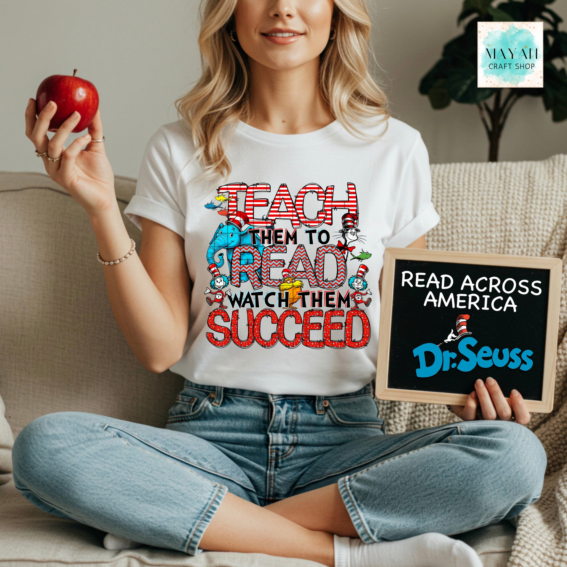 Person wearing a t-shirt with a quote, holding an apple and a sign, sitting on a couch.