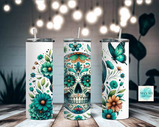 Three tumblers with floral and skull designs on a wooden surface with blurred lights in the background.