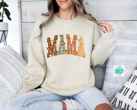 Woman wearing a cream sweatshirt with 'MAMA' printed on it, sitting on a wooden floor.