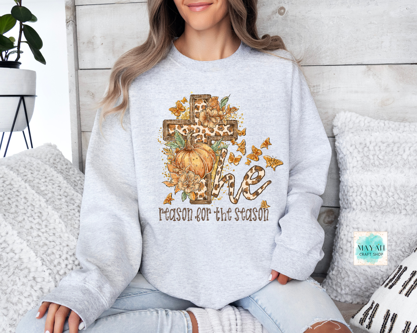 Person wearing a light gray sweatshirt with a pumpkin and cross design, sitting on a couch.