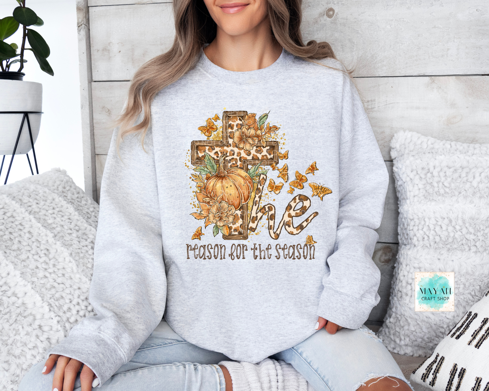 Person wearing a light gray sweatshirt with a pumpkin and cross design, sitting on a couch.