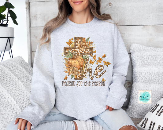 Person wearing a light gray sweatshirt with a pumpkin and cross design, sitting on a couch.