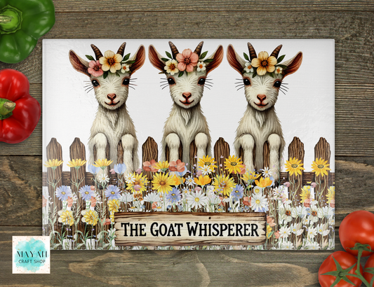 Poster with three goats wearing flower crowns and a sign 'The Goat Whisperer' on a wooden surface.