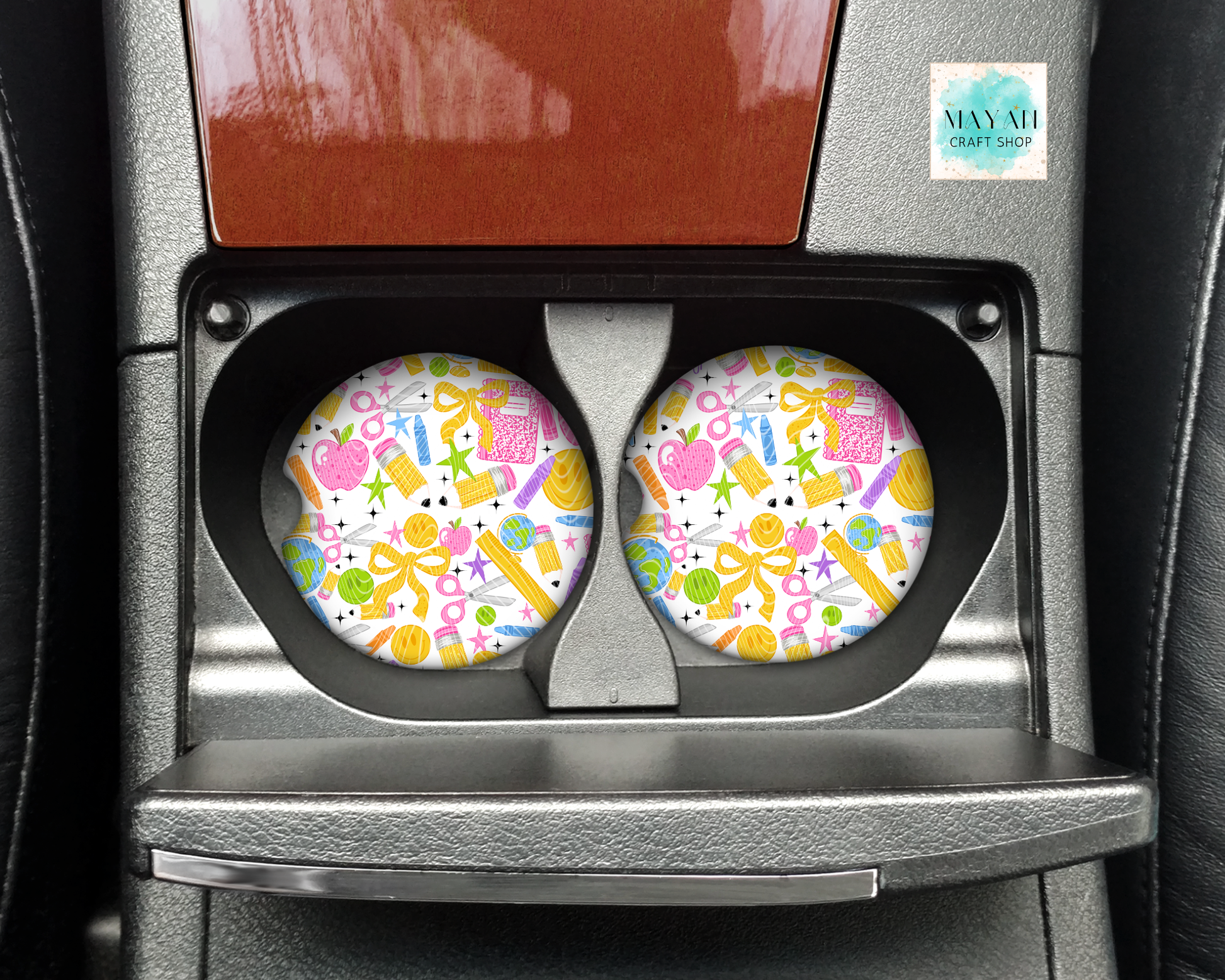 A pair of round car cup holders with colorful school-themed coasters inside a gray car center console.