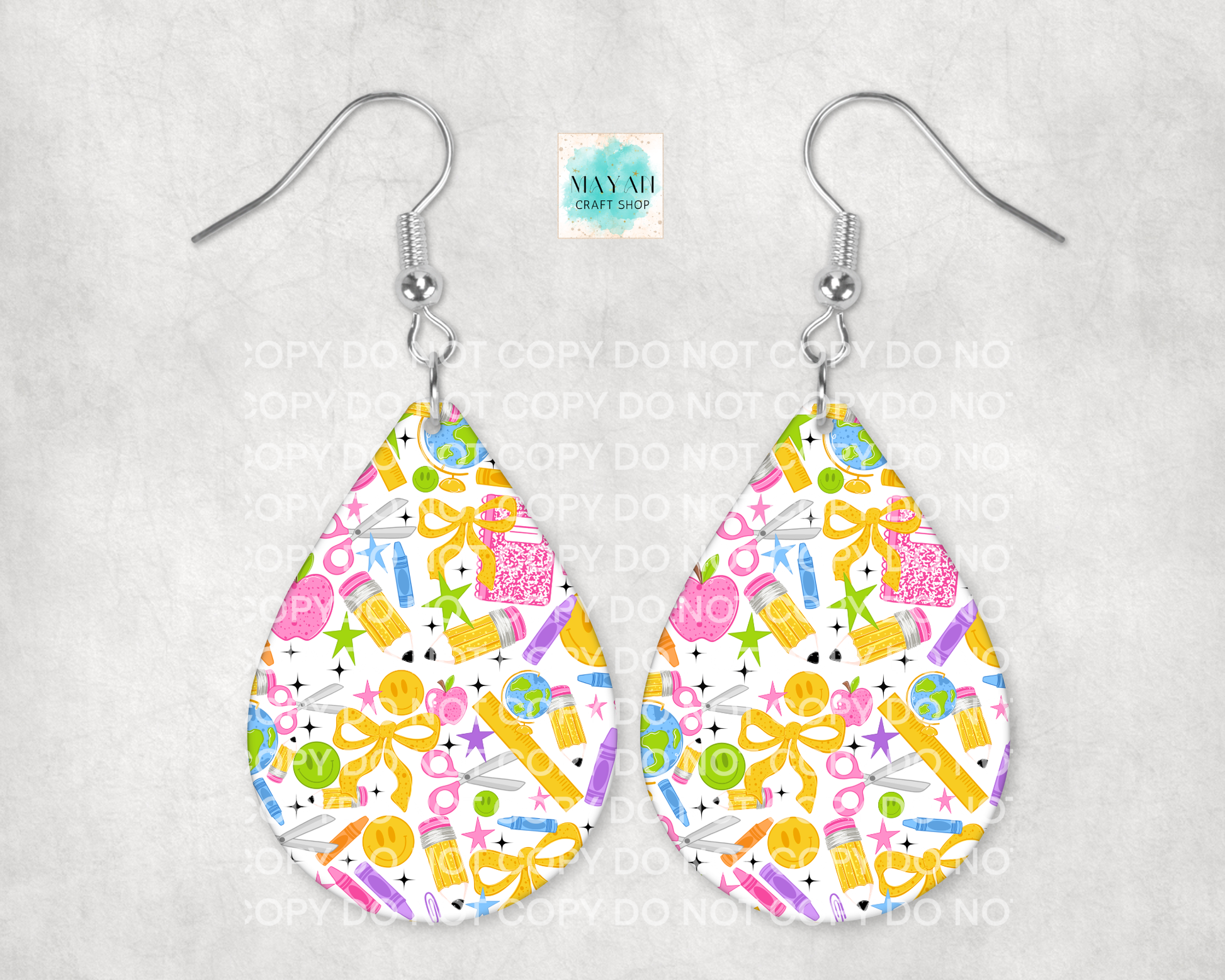 A pair of teardrop-shaped dangle earrings with a colorful pattern of notebooks, bows, stars, and apples on a white background, hanging from silver fishhook wires.