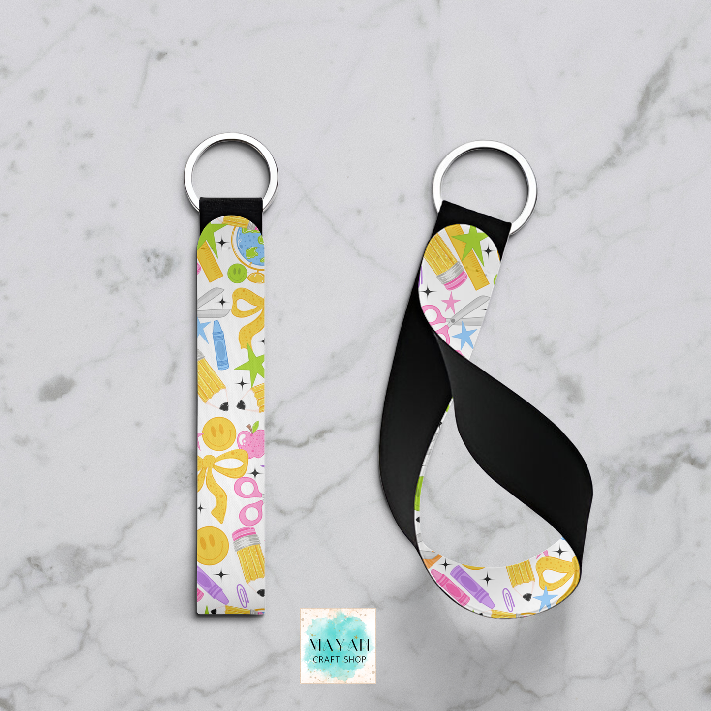 Two fabric keychains with silver metal key rings, displayed on a light gray marble background. One keychain is shown flat, and the other is twisted to display the strap's flexibility.