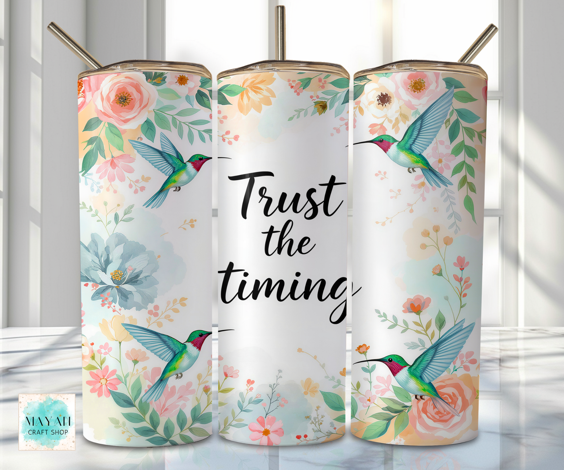 Three floral tumblers with hummingbird designs and 'Trust the timing' text on a light background.