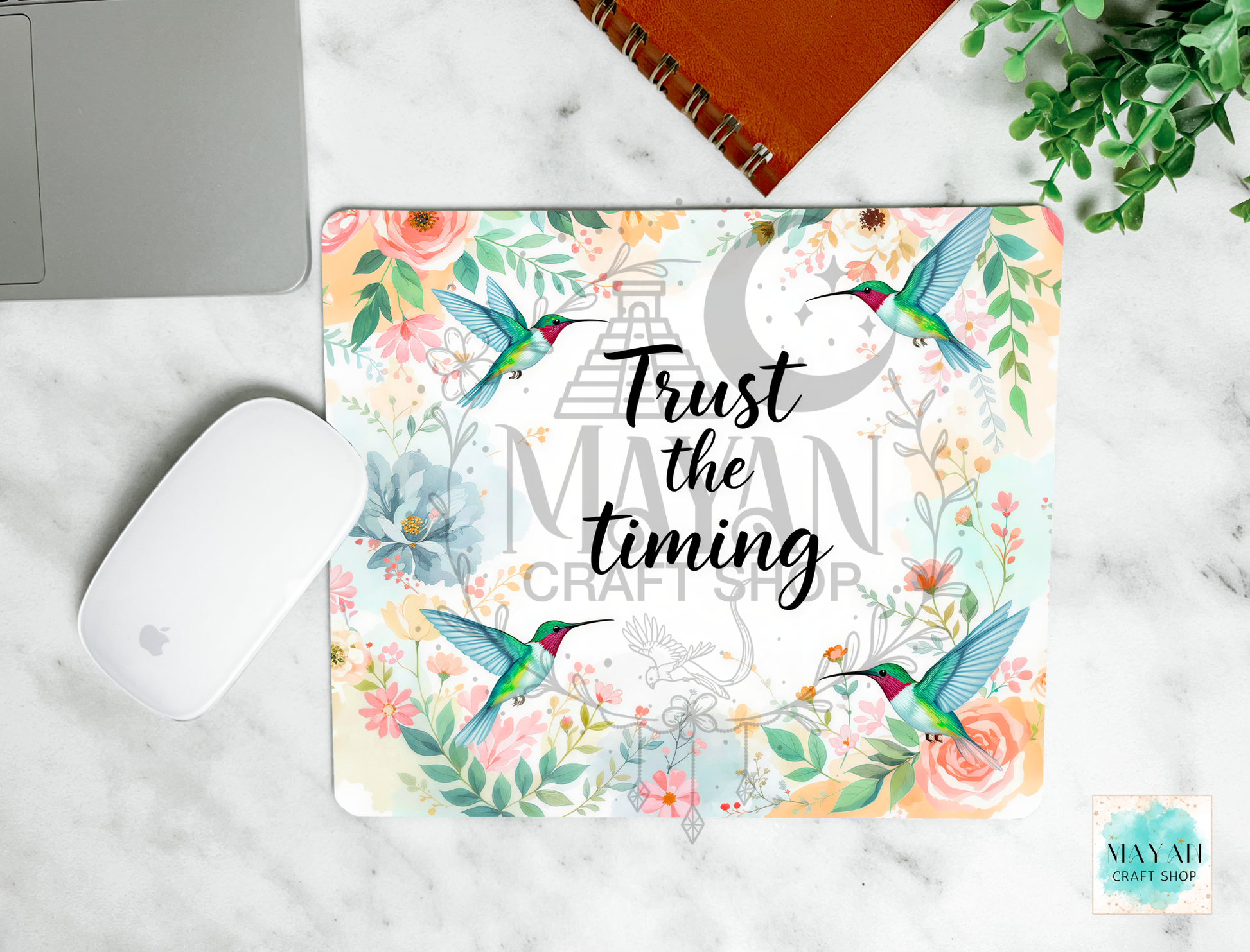 Floral mouse pad with hummingbirds and text 'Trust the timing' on a marble surface.