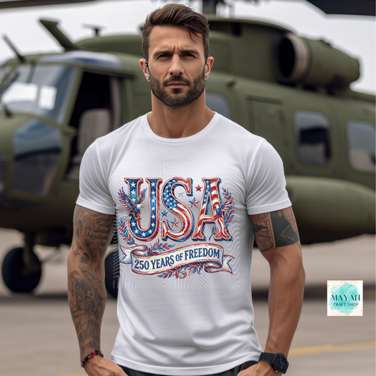 Man wearing a white t-shirt with 'USA 250 Years of Freedom' design in front of a helicopter.