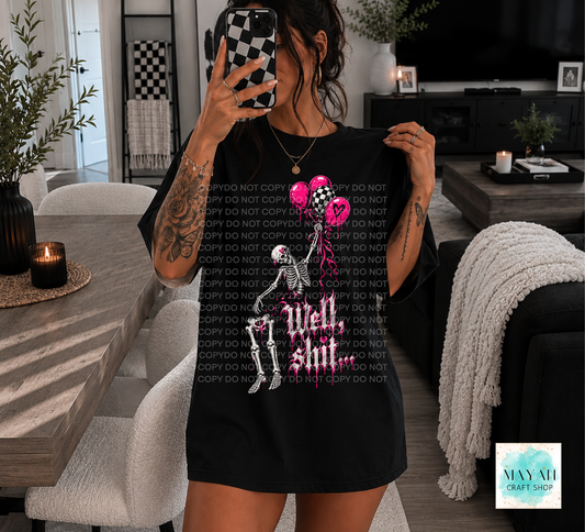 A woman takes a mirror selfie in a modern living room while wearing a black graphic t-shirt. The shirt features a skeleton and a pink ribbon design with the text 'Well shit' in a stylized font.