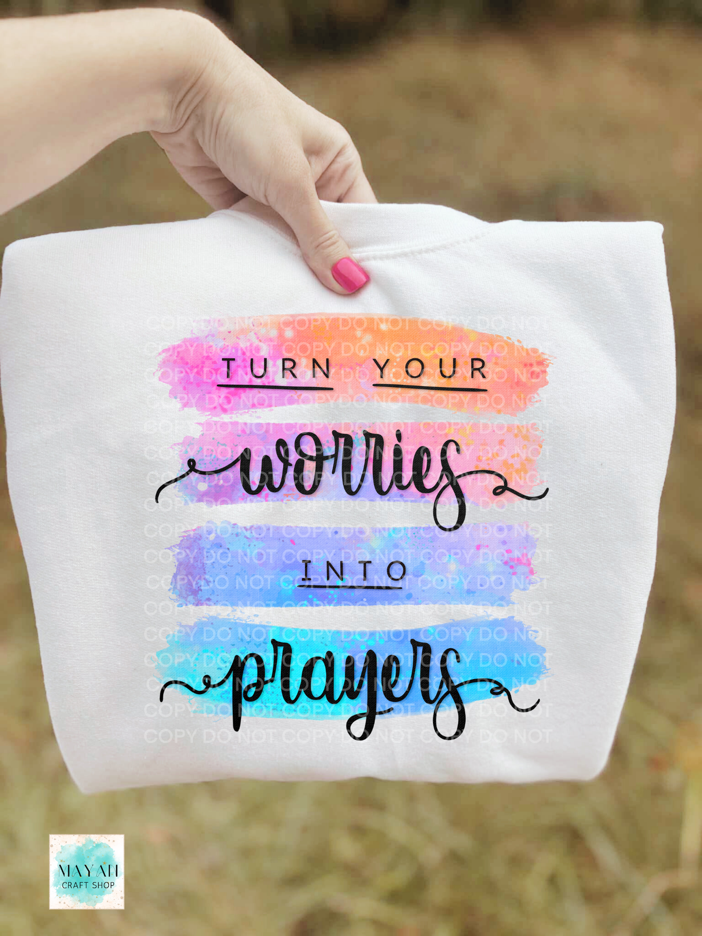White sweatshirt with colorful text 'Turn your worries into prayers' held by a hand.