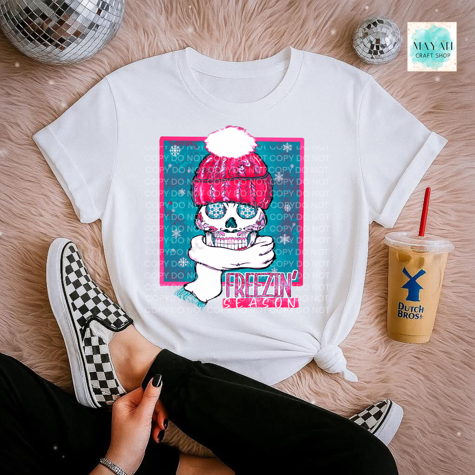 White t-shirt with a colorful graphic of a skull wearing a pink beanie, sitting on a pink surface with a drink and disco balls.