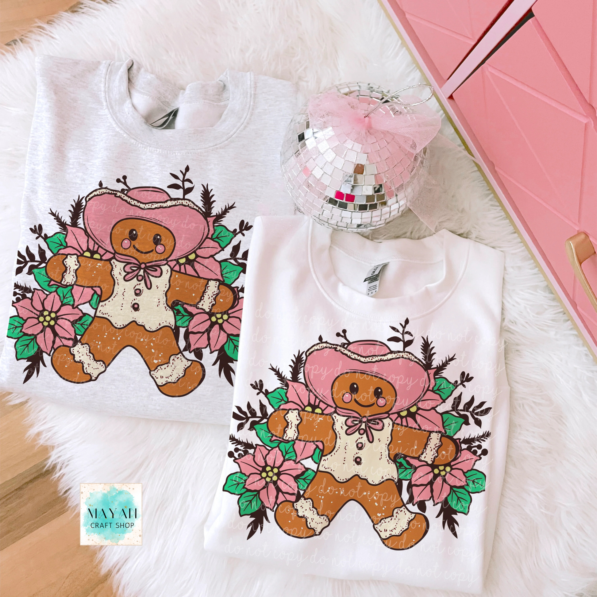 Two sweatshirts with gingerbread man designs on a fluffy white surface.