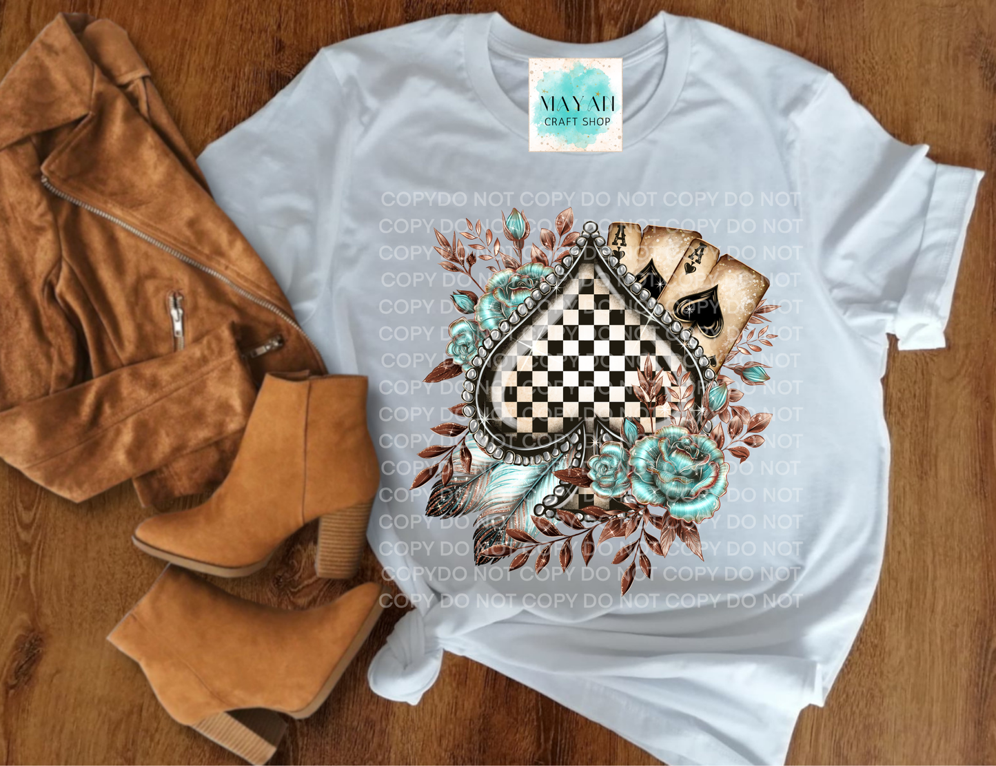White t-shirt with decorative design on a wooden surface with brown jacket and boots.