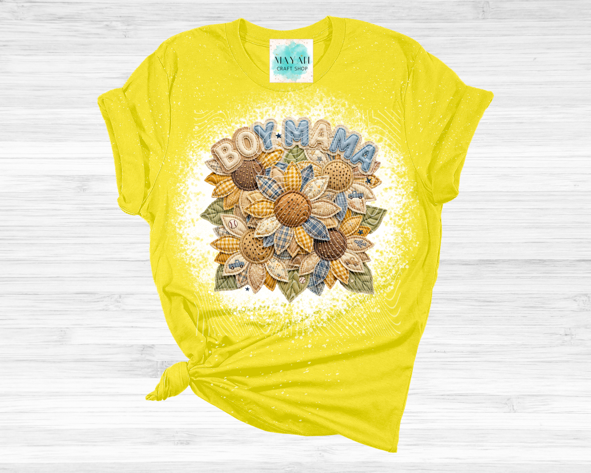 Yellow t-shirt with 'BOY MAMA' text and floral design on a wooden surface