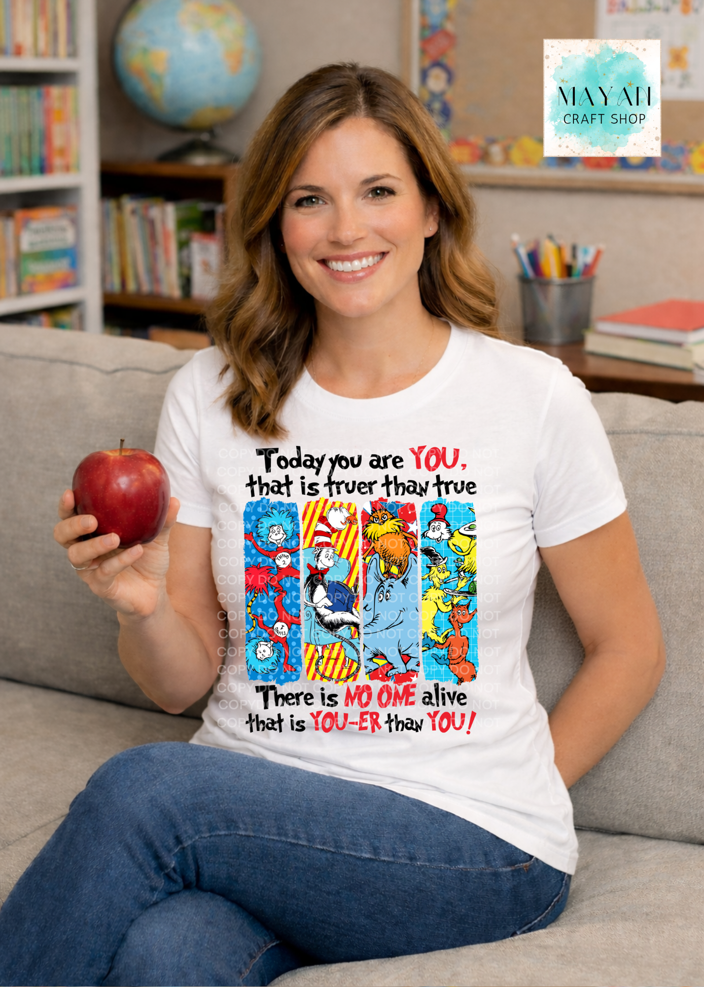 Woman sitting on a couch holding an apple, wearing a white t-shirt with colorful text and graphics.